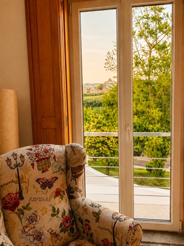 An armchair beside the living-room balcony doors, looking out over trees at golden hour